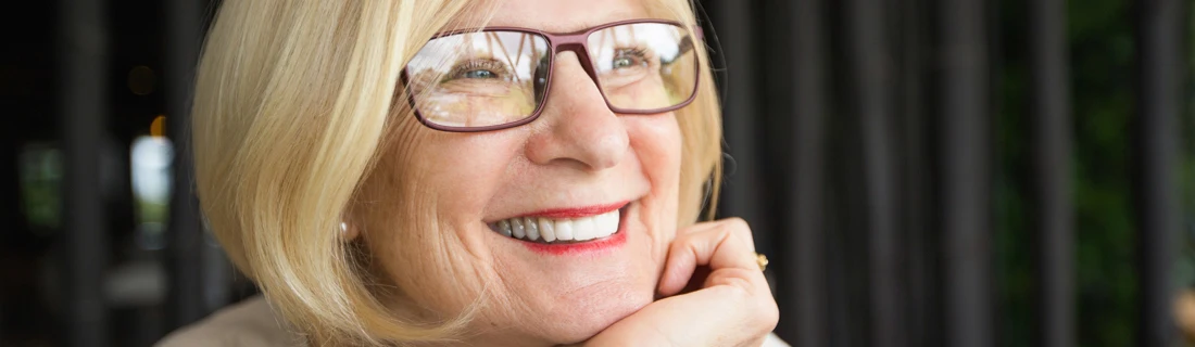 an older woman is smiling looking off in the distance leaning on her hand under her jaw
