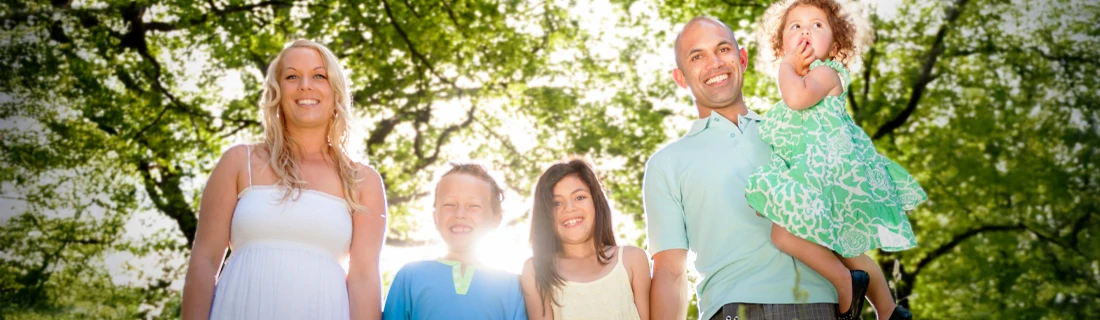 a happy family with a mother, father and three kids, is outside under trees holding hands