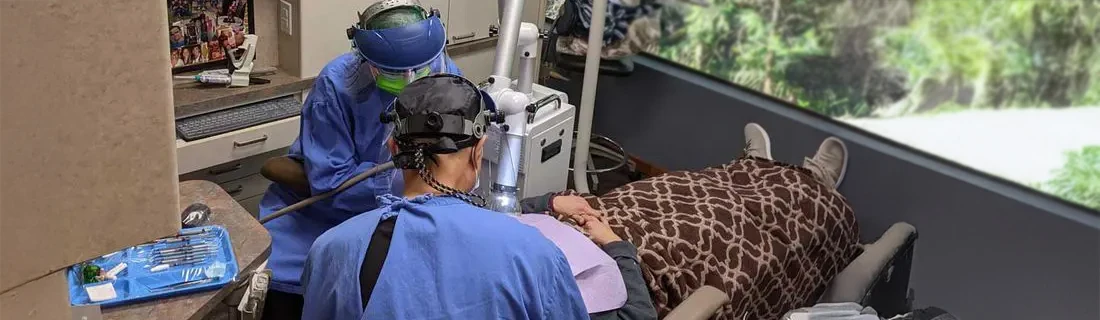 Dentist and assistant are working on a patient while they're wearing surgery garb